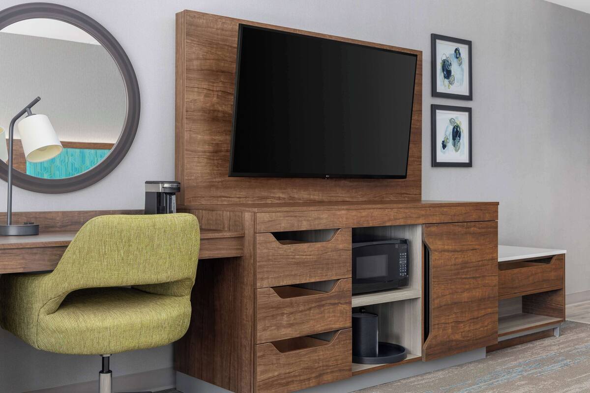 Una sala de estar moderna con un televisor de pantalla plana, un mueble de entretenimiento de madera, un sillón tapizado en verde y un espejo redondo.