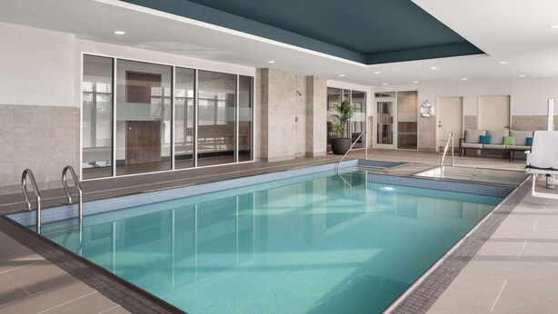 A modern indoor swimming pool with clear blue water, glass doors, and a seating area with a sofa and chairs. - Hampton Inn by Hilton Kingston (Kingston)
