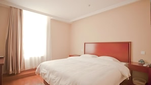 Una habitación de hotel con una cama grande, una mesita de noche de madera, una mesita auxiliar y una ventana con cortinas.