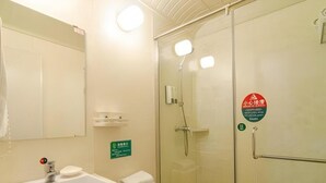 Un baño con lavabo, inodoro y ducha con mampara de cristal. Hay un cartel en la pared y un perchero.