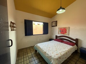 Una camera da letto con un letto, una finestra con persiane, un radiatore a parete, un quadro con un fiore rosso e una luce a soffitto.