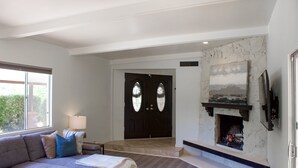 A living room with a grey sofa, a wooden coffee table, a fireplace, and a TV mounted on the wall.