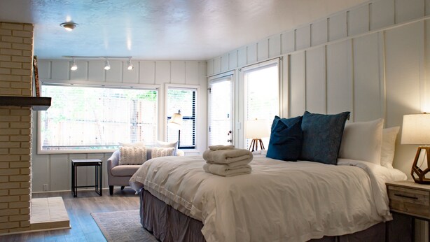 A bedroom with a large bed, a nightstand, a chair, and a window with blinds.