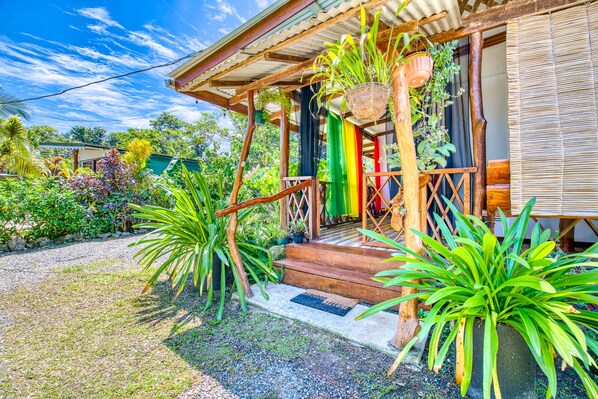 Una casa de madera con porche, rodeada de plantas tropicales y un camino de grava.
