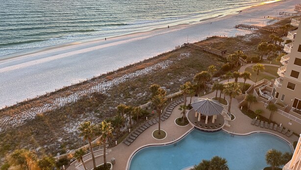 A resort with a swimming pool, beach access, and a view of the ocean at sunset.