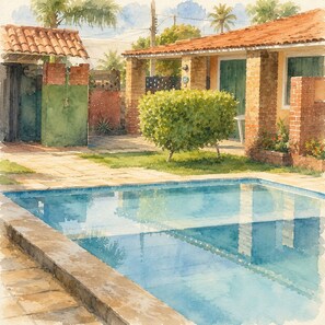 A swimming pool with a tiled edge, a brick house with a tiled roof, and a green bush.