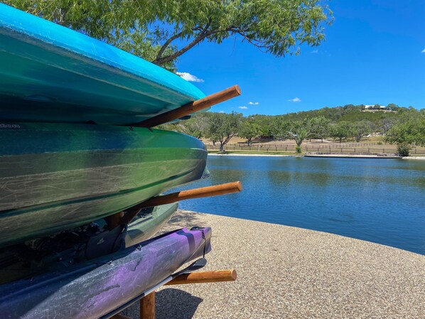 A row of kayaks on a pebbled shore with a lake and trees in the background.