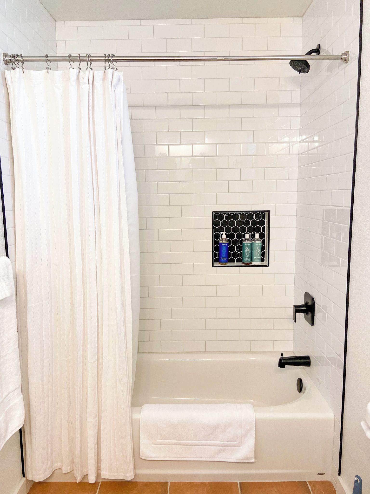 A bathroom with a white bathtub, a shower, and a tiled wall.
