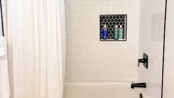 A bathroom with a white bathtub, a shower, and a tiled wall.