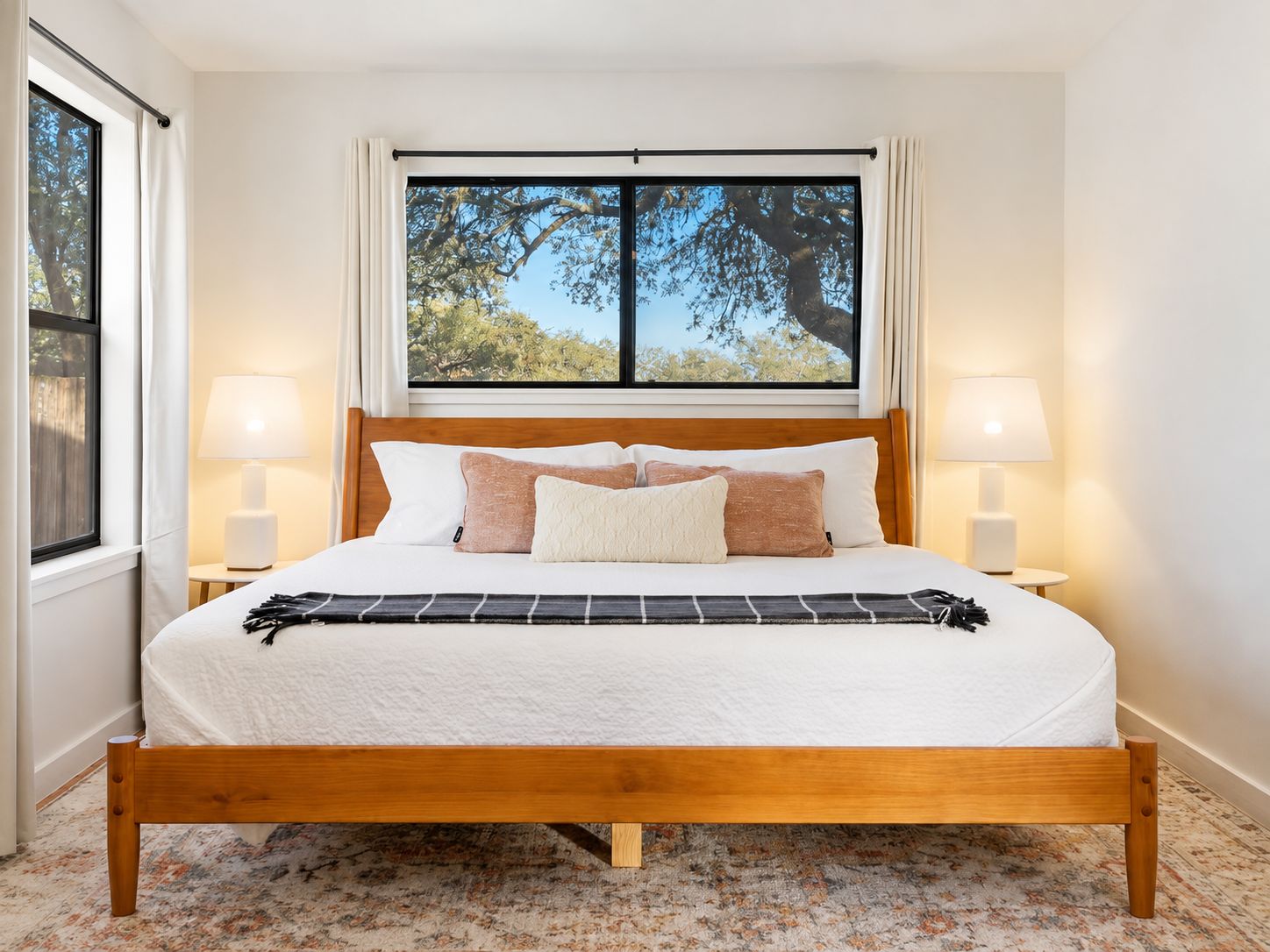 A neatly made bed with a wooden frame, white bedding, and a view of trees through a window.