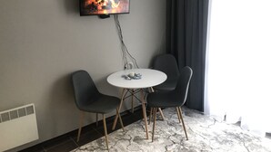 A room with a TV mounted on the wall displaying a fireplace, a round table with chairs, and a window with curtains. - MH Apartaments (Bansko)