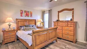 Un dormitorio con cama de madera, mesitas de noche, cómoda, ventilador de techo y dos cuadros en la pared.