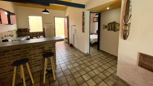 A kitchen with a central island, stools, a tiled floor, and a view into a bedroom.