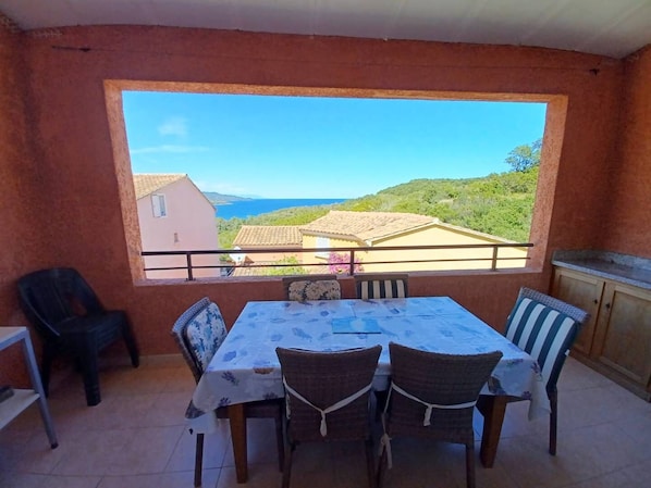 A balcony with a table and chairs, a view of houses and hills, and a clear sky.