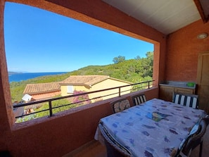 A balcony with a table and chairs, overlooking a coastal landscape with houses and greenery.