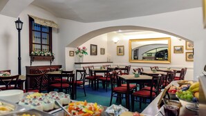 A dining area with multiple tables and chairs, a buffet with various food items, and a large mirror on the wall. - Orion (Prague)