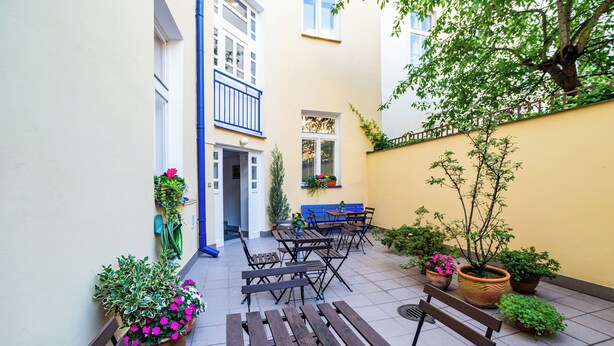 A courtyard with outdoor seating, potted plants, and a building entrance. - Orion (Prague)