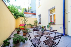 Un patio con plantas en macetas, bancos de madera y un pequeño parque infantil.