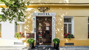 A hotel entrance with a sign, double doors, and potted plants. - Orion (Prague)