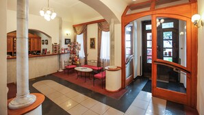 A lobby with a reception desk, a seating area with a table and chairs, a large column, and a wooden door with glass panels. - Orion (Prague)