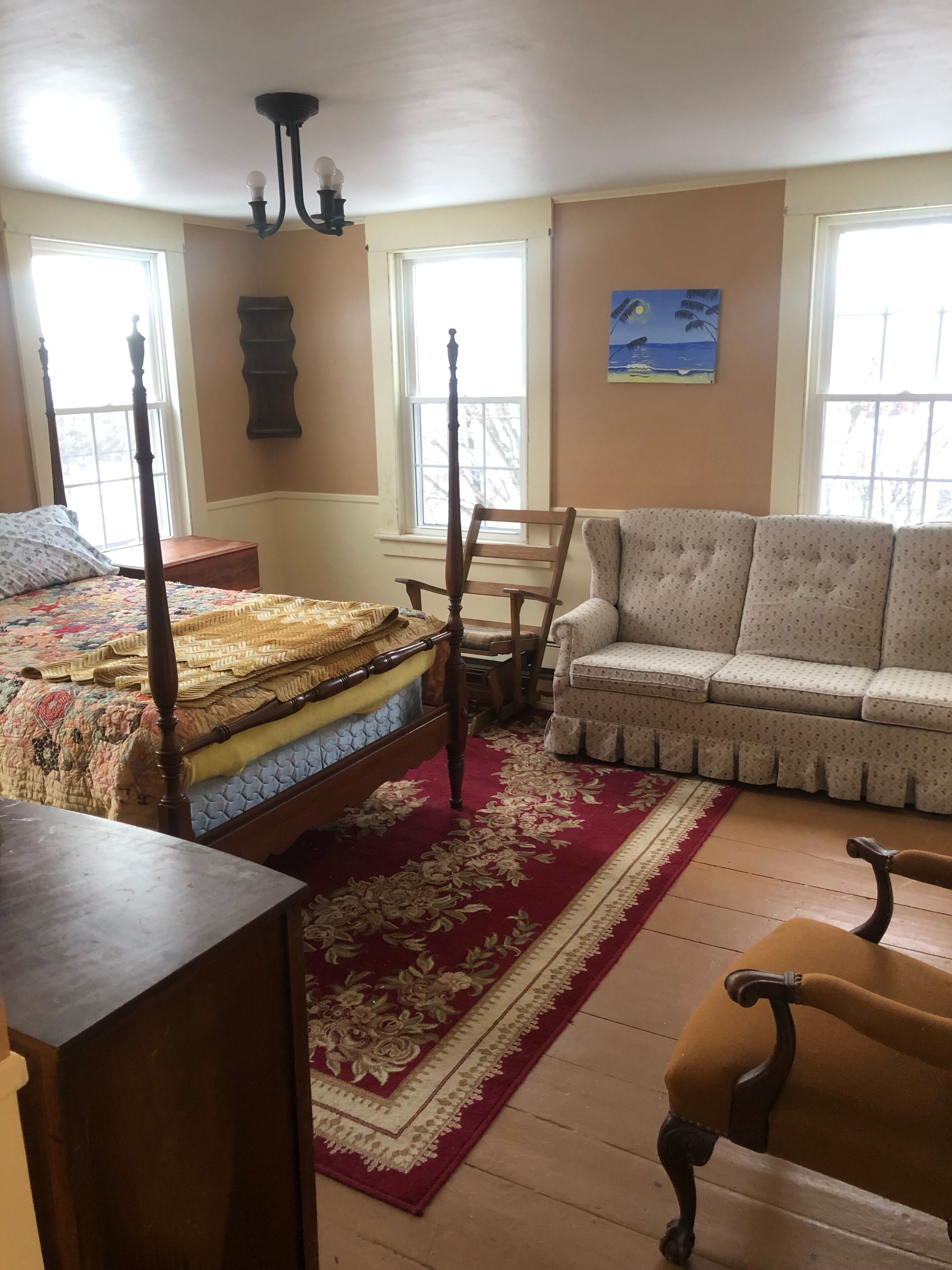 A bedroom with a four-poster bed, a sofa, a chair, and a table.