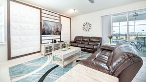Een moderne woonkamer met een bruine leren bank, een houten salontafel en een groot raam met uitzicht op de omgeving.