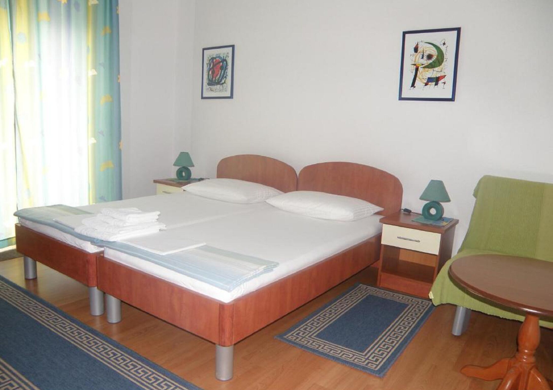 A hotel room with a wooden bed, two bedside tables with lamps, a green chair, and a small round table.