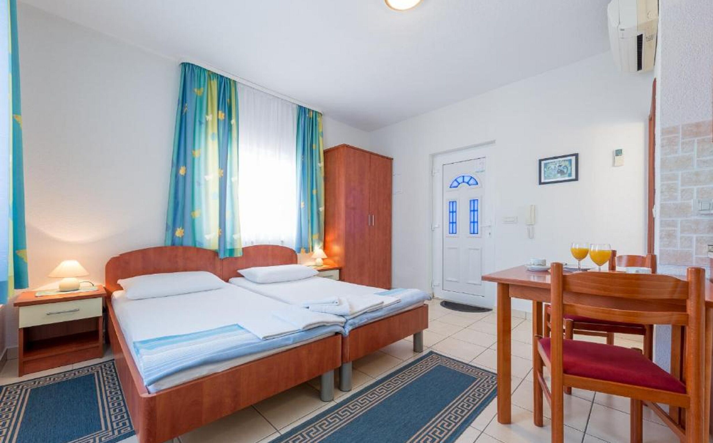 A hotel room with a double bed, a wooden wardrobe, a desk with a chair, and a bathroom door.