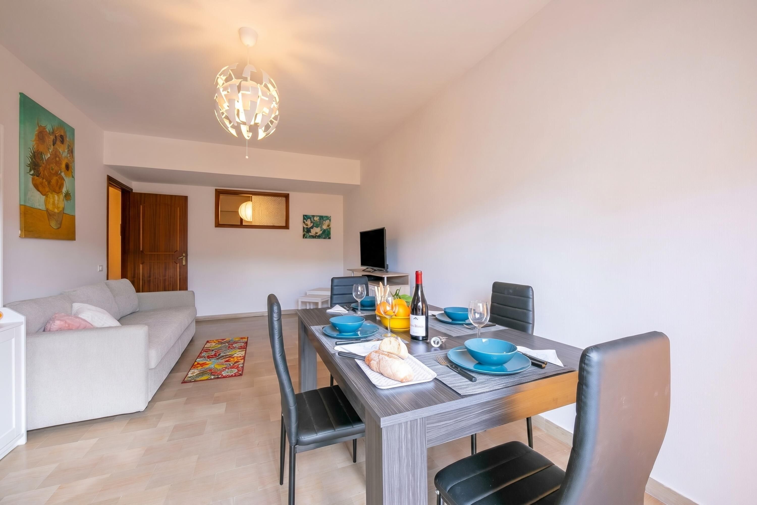 Un comedor con una mesa para dos, un sofá, un televisor y una puerta que da a otra habitación.