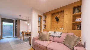 A cozy living room with a pink sofa, wooden shelves, and a dining area with a table and chairs. - Menina (Livigno)
