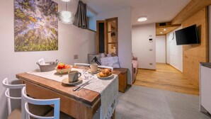 A cozy dining area with a wooden table, white chairs, and a large painting of a forest. - Menina (Livigno)
