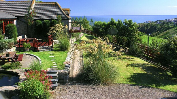 Una casa costera con fachada de piedra, una terraza de madera y vistas al mar.