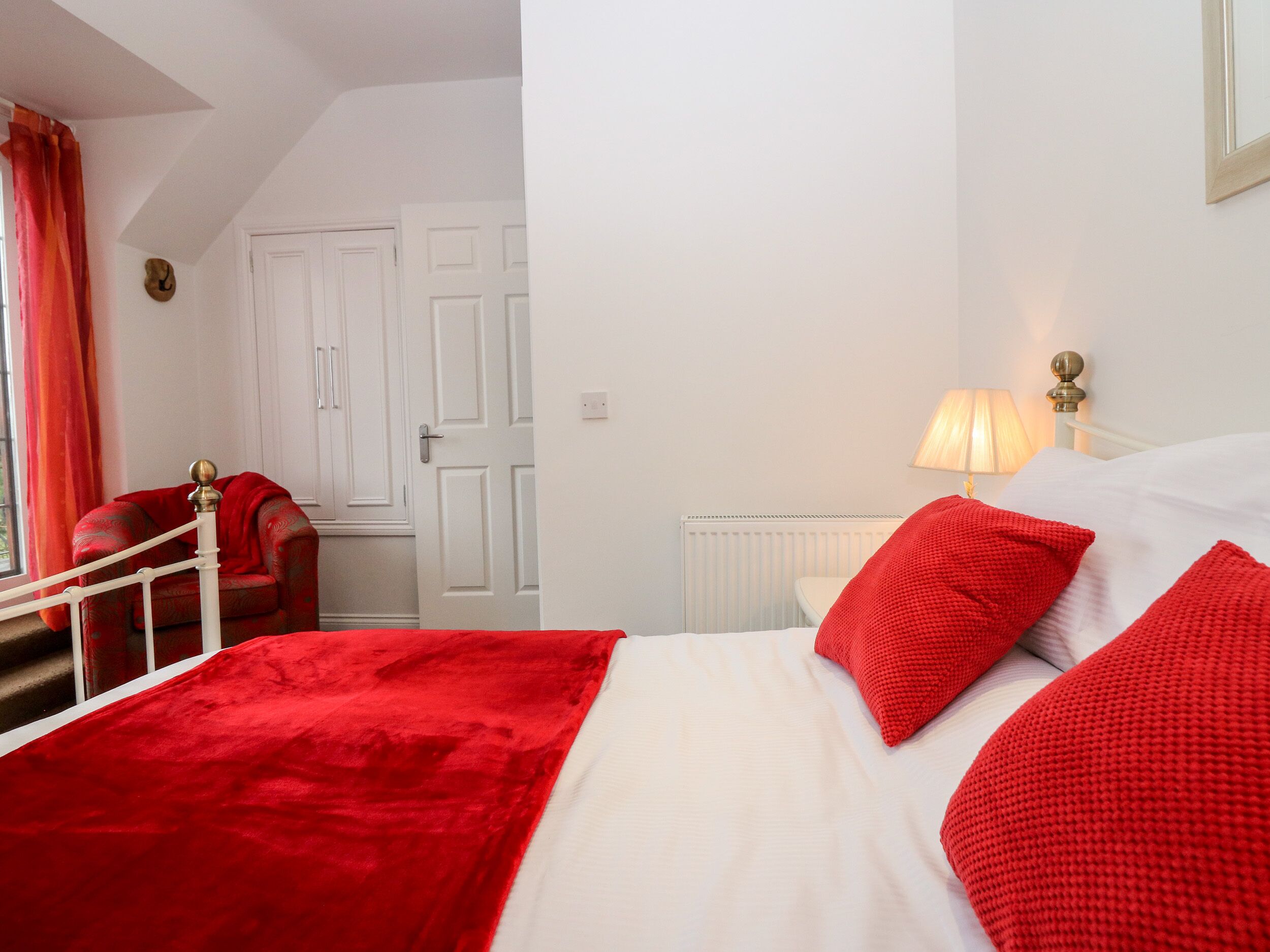 Een hotelkamer met een bed, rode kussens, een rode stoel, een witte radiator en een deur.