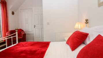 Een hotelkamer met een bed, rode kussens, een rode stoel, een witte radiator en een deur.
