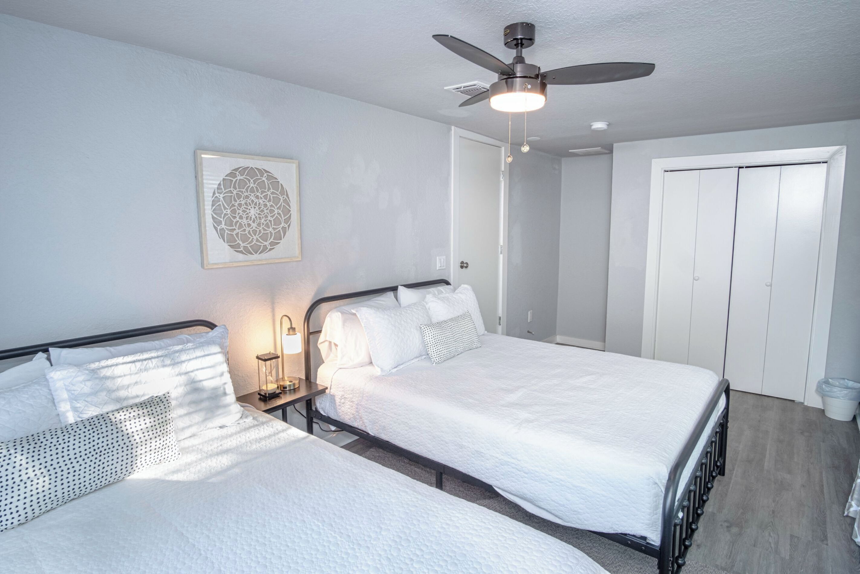A bedroom with two beds, a ceiling fan, a wall-mounted light, and a door.