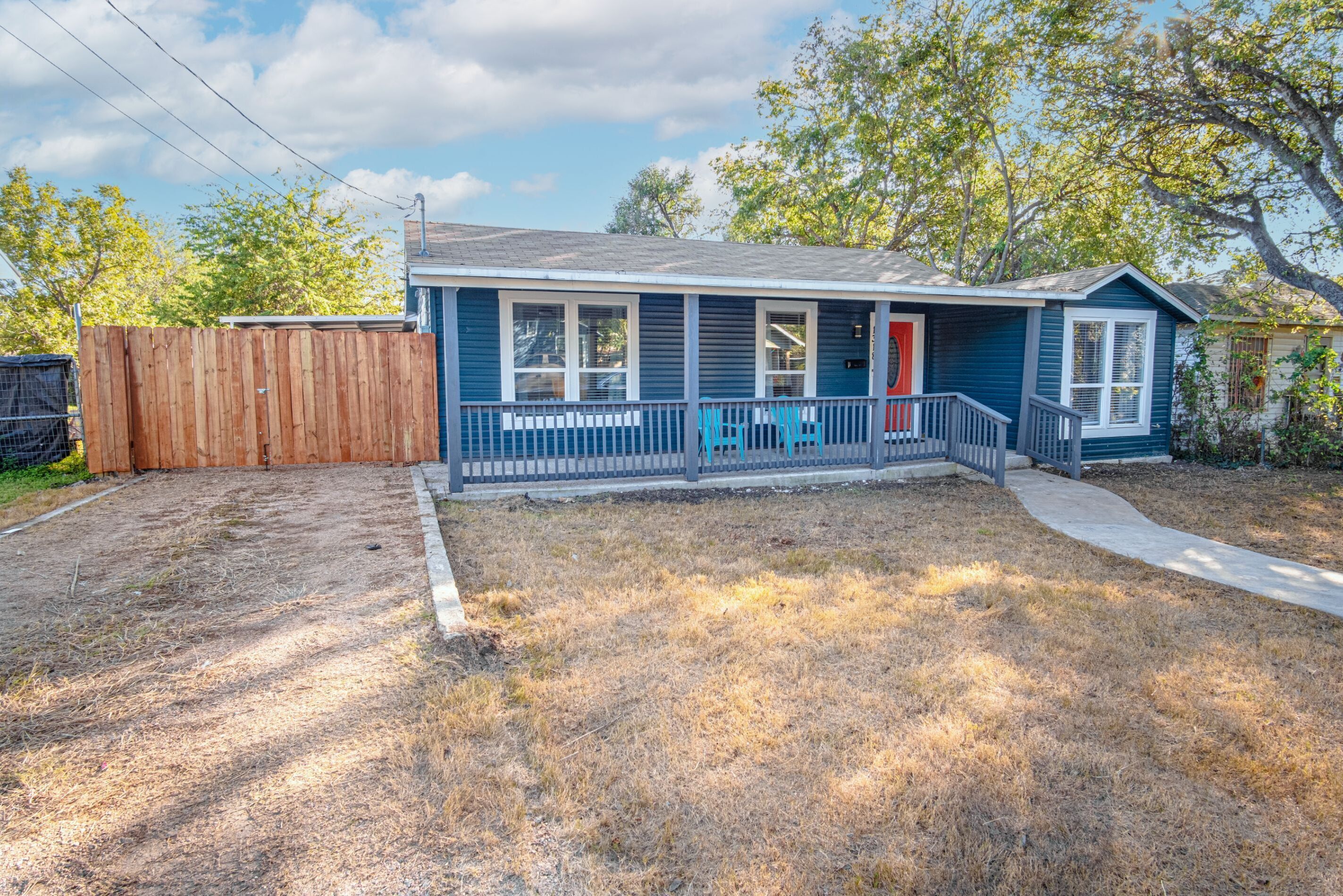 A single-story house with a blue exterior, a front porch, and a wooden fence.