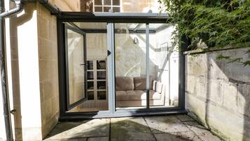 A glass door leading to a room with a sofa and a small table, a stone wall, and a plant.