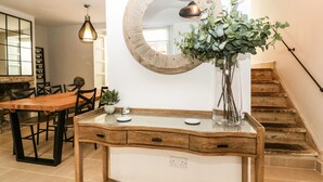 Een eethoek met een houten tafel, stoelen, een vaas met groen, een wandspiegel en een hanglamp.