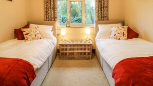 Habitación doble con dos camas, una ventana con cortinas, una mesita de noche con lámparas y un pequeño cofre de madera.