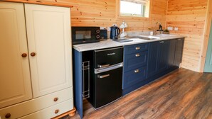 Cocina pequeña con paredes de madera, microondas, cafetera y lavavajillas.