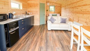 Una cabaña de madera compacta con kitchenette, comedor y sala de estar con sofá y sillones.