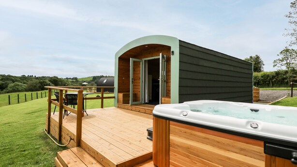 Una terraza de madera con un jacuzzi y un pequeño edificio con la puerta abierta.