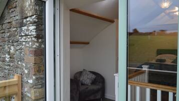 A room with a stone wall, a wooden bench, and a dark-colored armchair with a pillow.