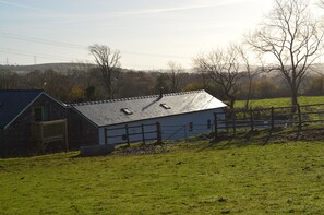 A rural barn with a sloped roof, surrounded by a fenced pasture and trees. - Cwrt y Wennol (Swansea)