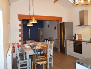 A compact kitchen with a dining area, a built-in oven, and a stainless steel refrigerator. - Cwrt y Wennol (Swansea)