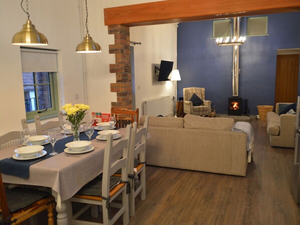 A dining area with a table set for four, a sofa, and a fireplace. - Cwrt y Wennol (Swansea)