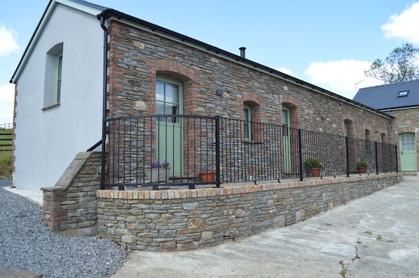 A stone building with a white facade, green doors, and a black metal fence. - Cwrt y Wennol (Swansea)