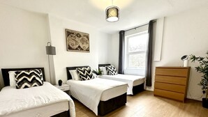 A bedroom with two beds, a dresser, a lamp, a window with curtains, and a wall-mounted globe. - Beautiful 3-bed Apartment With Driveway Parking (Nottingham)