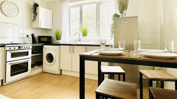 A modern kitchen with white appliances, a dining area with a wooden table and chairs, and a window with natural light. - Beautiful 3-bed Apartment With Driveway Parking (Nottingham)
