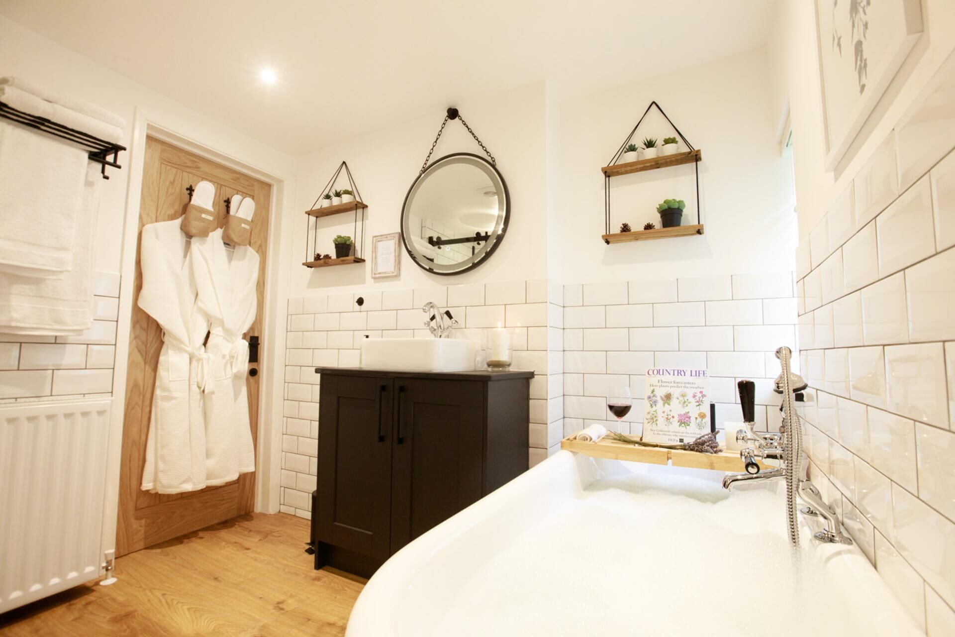 A bathroom with a bathtub, a sink, and a mirror. There are wooden cabinets and shelves with plants.